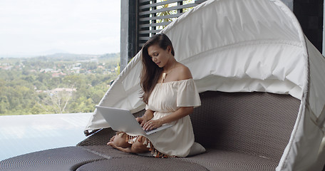 Image showing Adult barefooted woman using laptop on balcony against landscape at tropical resort