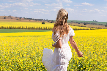 Image showing Woman in white dress looking out over fields of golden canola