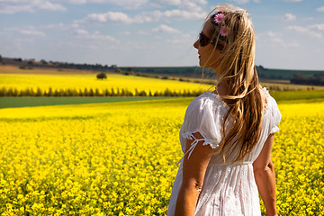 Image showing Woman in white dress standing by fields of golden canola