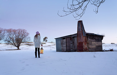 Image showing A woman standing in a snow field holding lantern at dusk