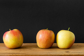 Image showing black background three apples wooden table
