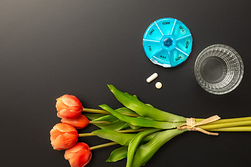 Image showing open pillbox with some pills glass of water and tulips