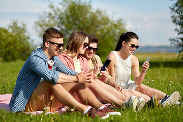 Image showing smiling friends with smartphones sitting on grass