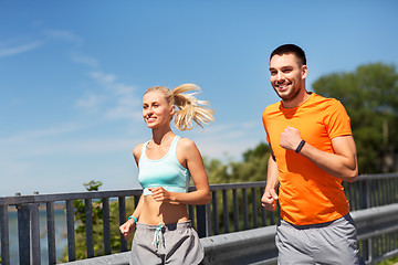 Image showing couple with fitness trackers running along bridge