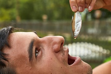 Image showing Holding a very small fish above open mouth