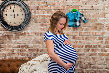 Image showing Beautiful pregnant woman sitting near wall