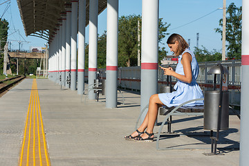 Image showing Young girl looks at the phone on the empty platform of the railway station