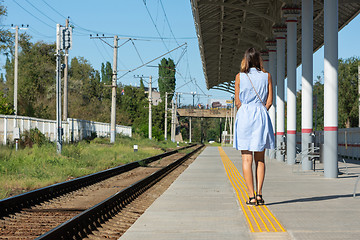 Image showing Young beautiful girl stands alone on a railway platform with her back to the camera
