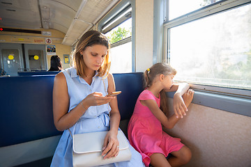 Image showing A young girl looks at the phone, daughter at the window in the electric train