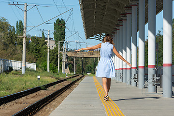 Image showing Young beautiful girl goes on the platform holding her arms outstretched to the side