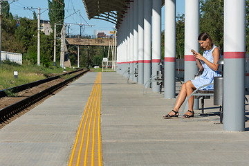 Image showing Young girl with a phone waits for a train on the empty platform of the railway station