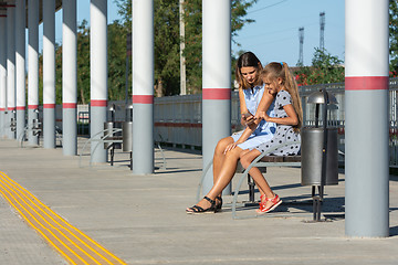 Image showing Mom and daughters wait for the train and look at the phone on the empty platform of the railway station