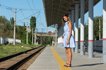 Image showing Young beautiful girl stands alone on a railway platform and looks into the distance with anticipation