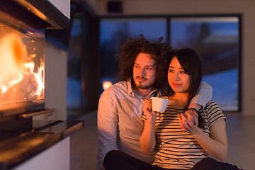 Image showing happy multiethnic couple sitting in front of fireplace