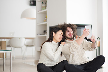 Image showing multiethnic couple using tablet computer in front of fireplace