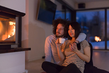 Image showing happy multiethnic couple sitting in front of fireplace