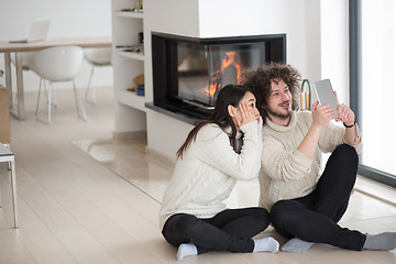 Image showing multiethnic couple using tablet computer in front of fireplace