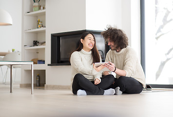 Image showing multiethnic couple using tablet computer in front of fireplace