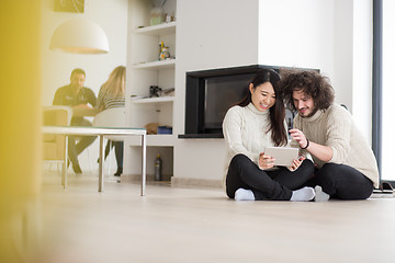 Image showing multiethnic couple using tablet computer in front of fireplace