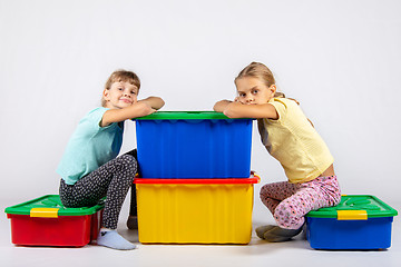 Image showing Two girls are sitting on large boxes for toys and looked into the frame