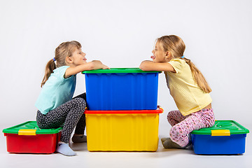 Image showing Two girls sit on big boxes for toys and show each other tongue