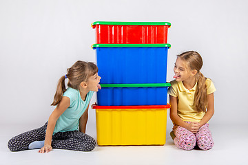 Image showing Two girls peek from different sides of large plastic boxes and show each other their tongues