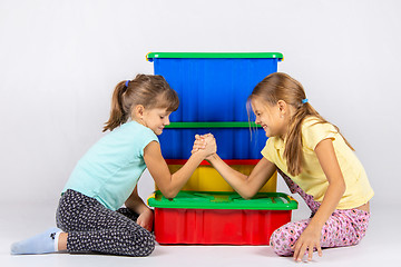 Image showing Two girls fight on hands, putting elbows on a box with toys