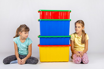 Image showing Two girls look at each other hiding behind large plastic boxes in the middle between them