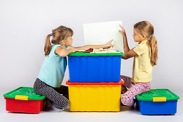 Image showing Two girls sit on large toy boxes and look at the toy assembly instructions