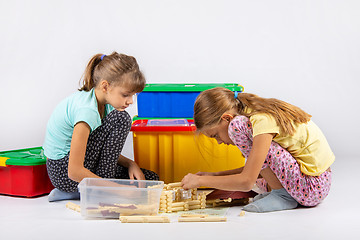 Image showing Two girls sit on the floor and collect a toy house