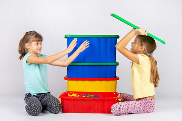 Image showing A girl pretending to be a hundred wants to throw a toy box lid on another girl