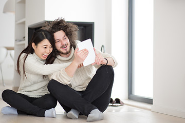 Image showing multiethnic couple using tablet computer in front of fireplace