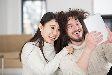 Image showing multiethnic couple using tablet computer in front of fireplace