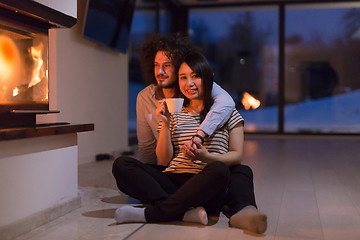 Image showing happy multiethnic couple sitting in front of fireplace