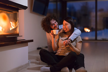 Image showing happy multiethnic couple sitting in front of fireplace