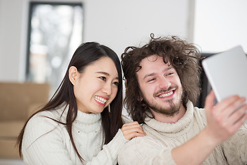 Image showing multiethnic couple using tablet computer in front of fireplace