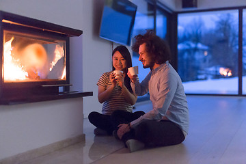 Image showing happy multiethnic couple sitting in front of fireplace