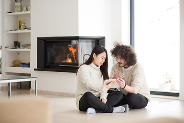 Image showing multiethnic couple using tablet computer in front of fireplace