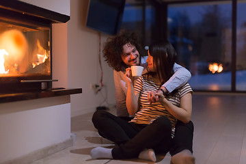 Image showing happy multiethnic couple sitting in front of fireplace