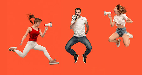 Image showing Beautiful young man and woman jumping with megaphone isolated over red background