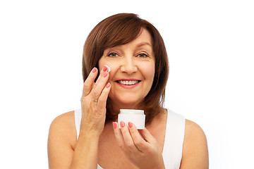 Image showing smiling senior woman applying cream to her face