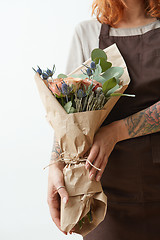 Image showing Female in a brown apron with red hair hold nice bouquet from living coral colored roses and eryngium on a light