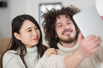 Image showing multiethnic couple using tablet computer in front of fireplace