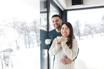 Image showing multiethnic couple enjoying morning coffee by the window