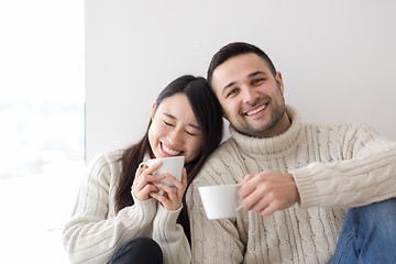 Image showing multiethnic couple enjoying morning coffee by the window