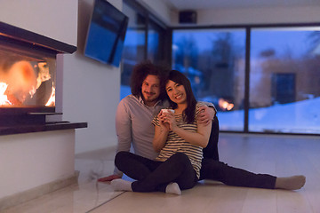 Image showing happy multiethnic couple sitting in front of fireplace