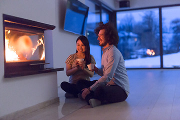 Image showing happy multiethnic couple sitting in front of fireplace