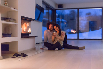 Image showing happy multiethnic couple sitting in front of fireplace