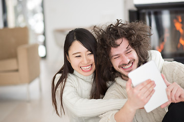 Image showing multiethnic couple using tablet computer in front of fireplace