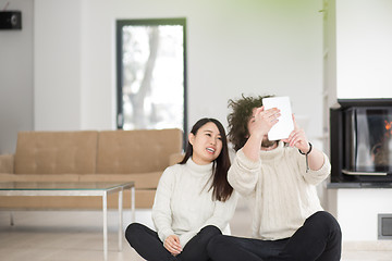 Image showing multiethnic couple using tablet computer in front of fireplace